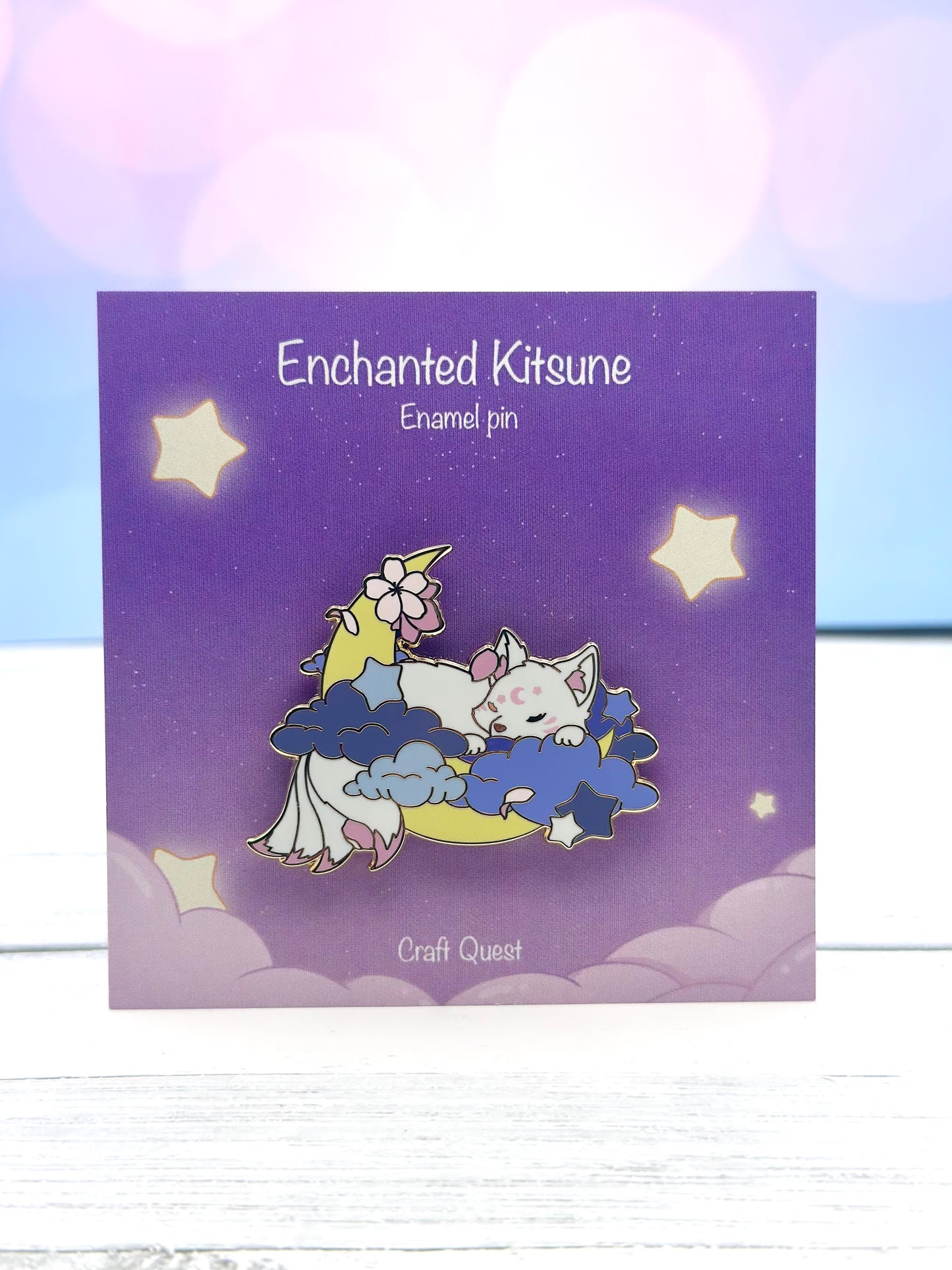 Enamel pin featuring a sleeping white kitsune resting on blue clouds and a crescent moon on a purple display card.