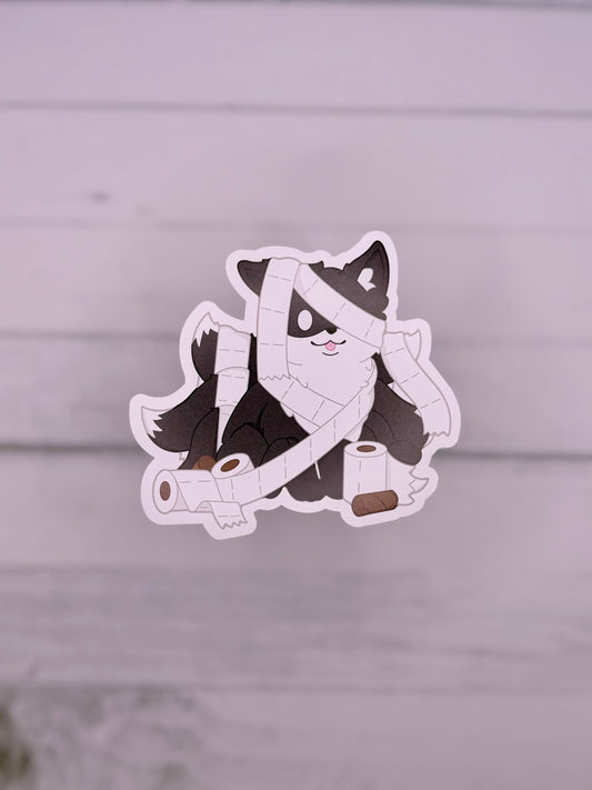 Black kitsune sticker wrapped in toilet paper like a playful mummy surrounded by toilet paper rolls