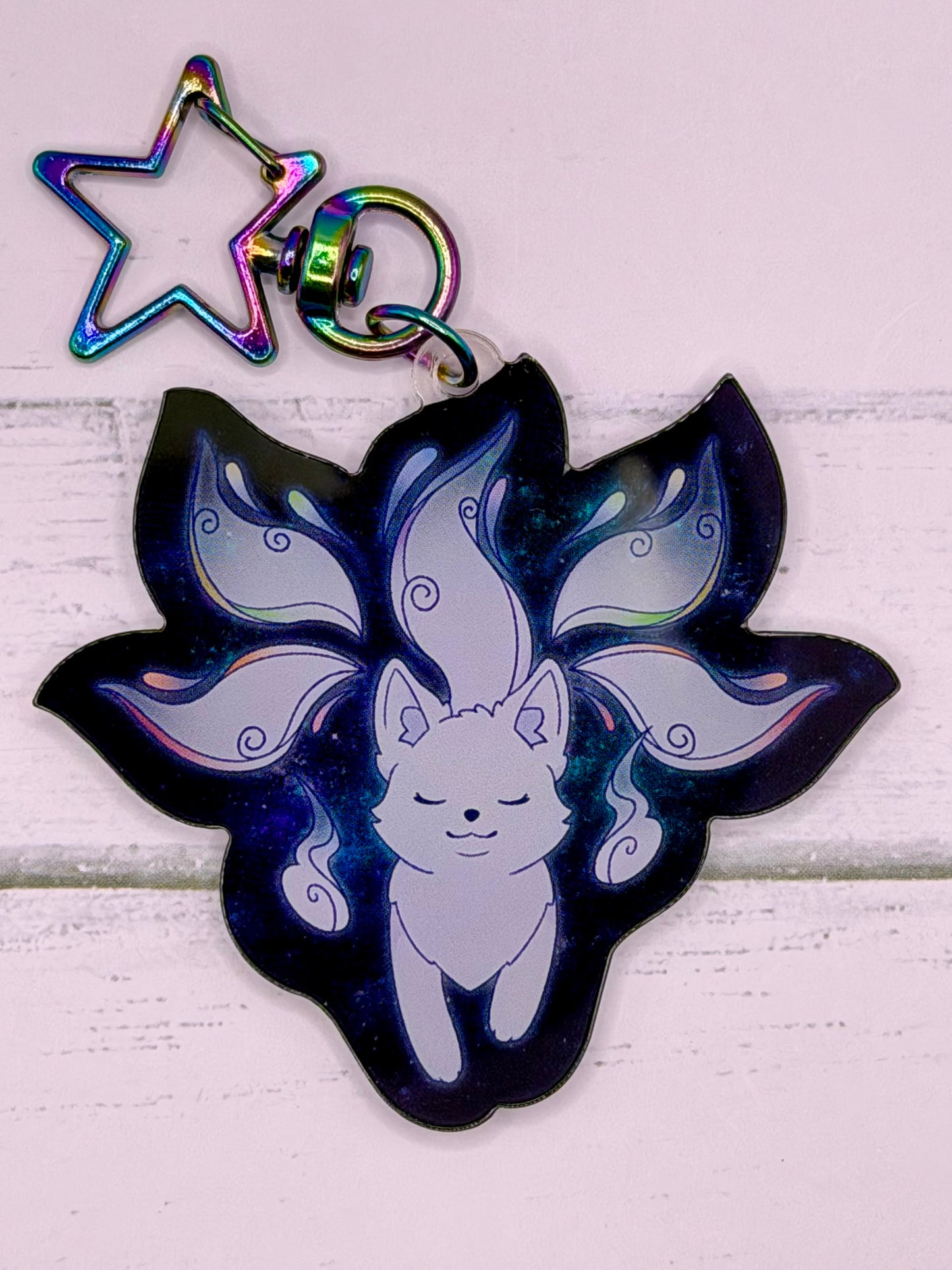 Galaxy themed acrylic kitsune keychain featuring a white fox spirit with flowing tails on a dark blue starry background and rainbow star clasp