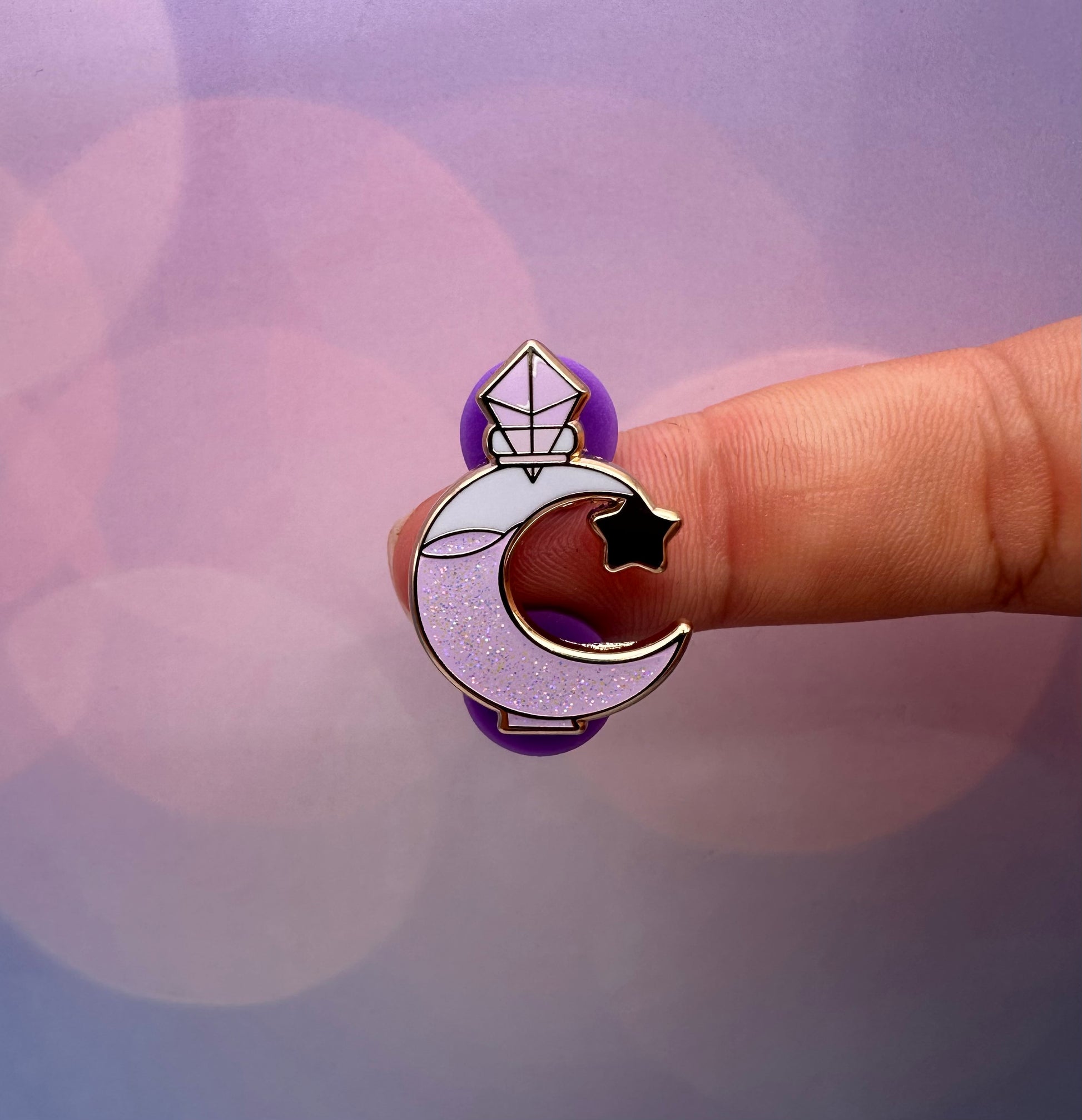 Hard enamel pin shaped like a crescent moon potion bottle filled with glittery lavender liquid and topped with a faceted crystal stopper