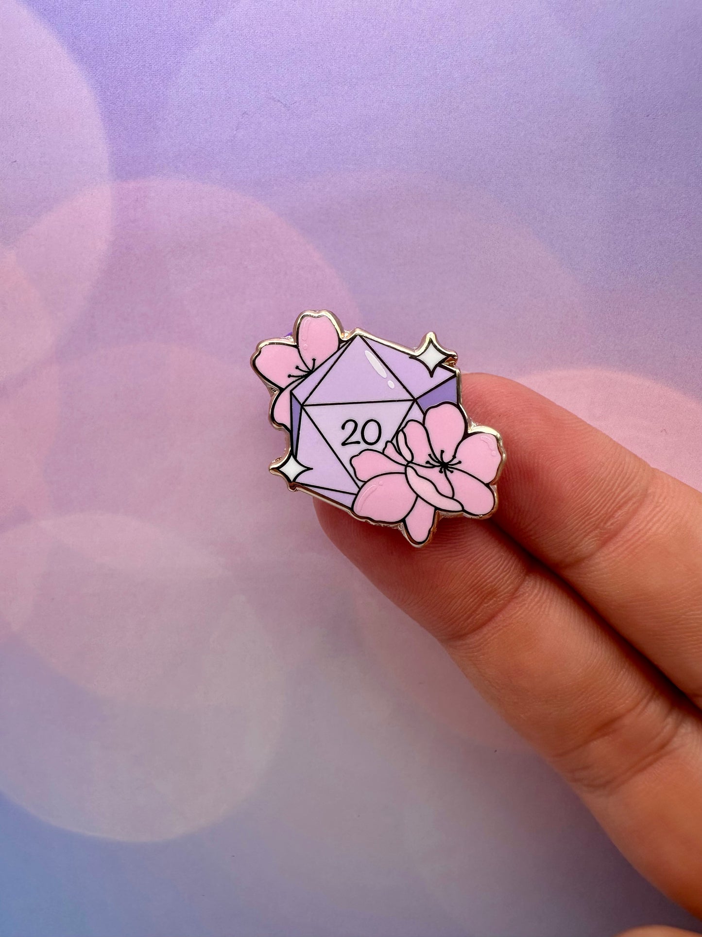 Pastel lavender twenty-sided dice enamel pin decorated with pink cherry blossoms and small sparkle accents