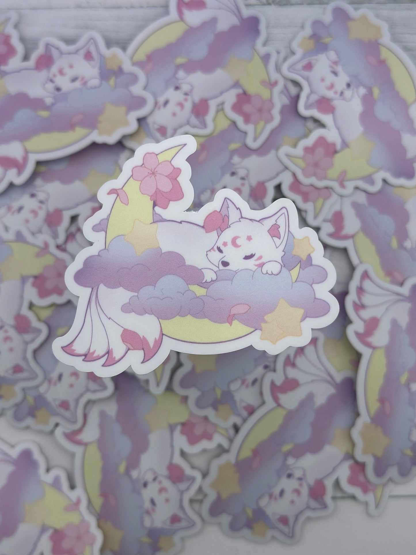 Cute pastel kitsune sleeping on lavender clouds beneath a crescent moon surrounded by stars and pink sakura petals
