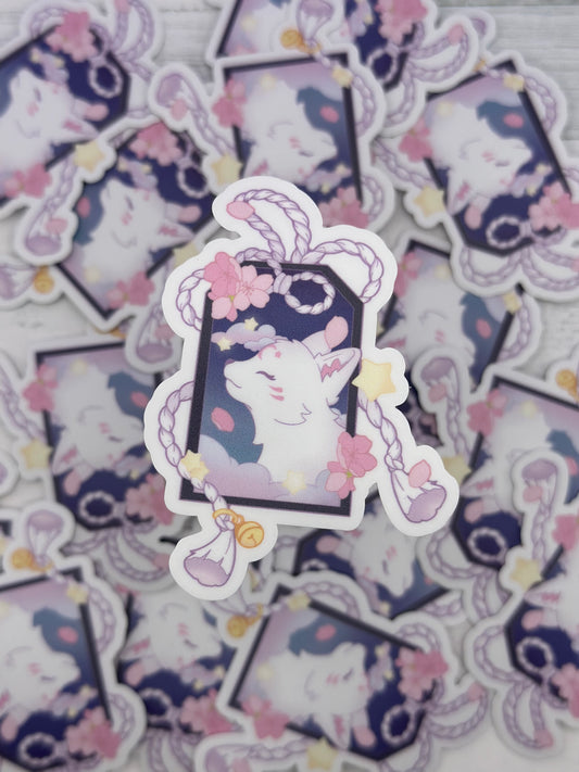 Pastel kitsune sticker framed inside a decorative tag with braided cords, bells, cherry blossoms, and floating stars