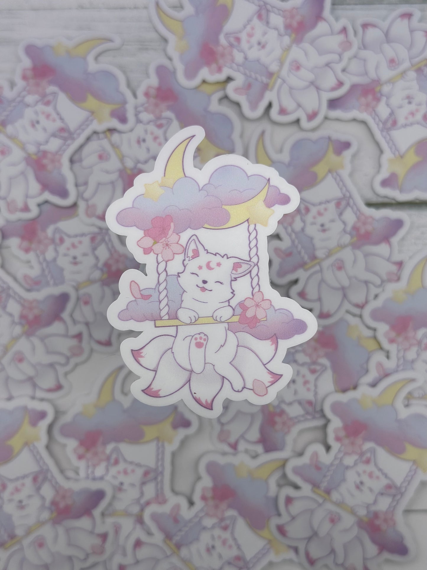 Cute pastel kitsune sitting on a swing suspended from clouds and a crescent moon with cherry blossoms and stars