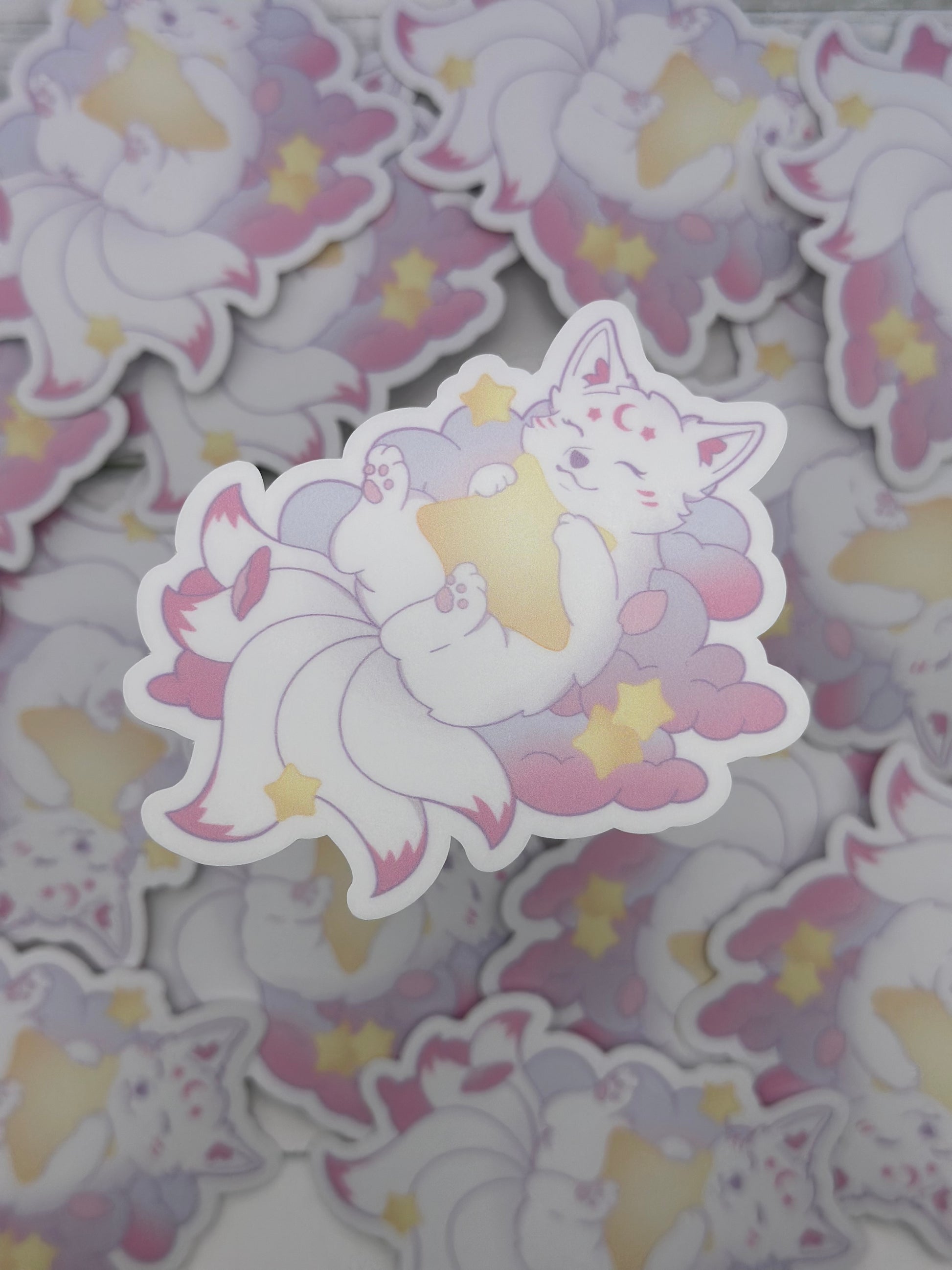 Pastel kitsune lying on fluffy clouds while hugging a glowing yellow star surrounded by small stars and petals