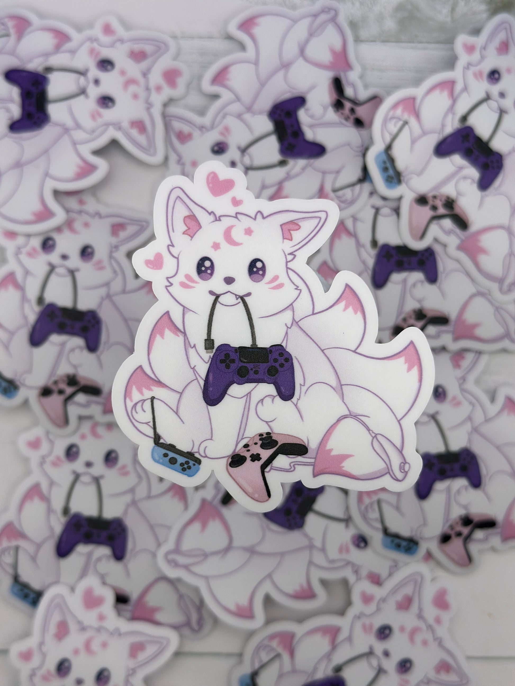 Cute pastel kitsune surrounded by colorful game controllers while holding a purple controller cord in its mouth