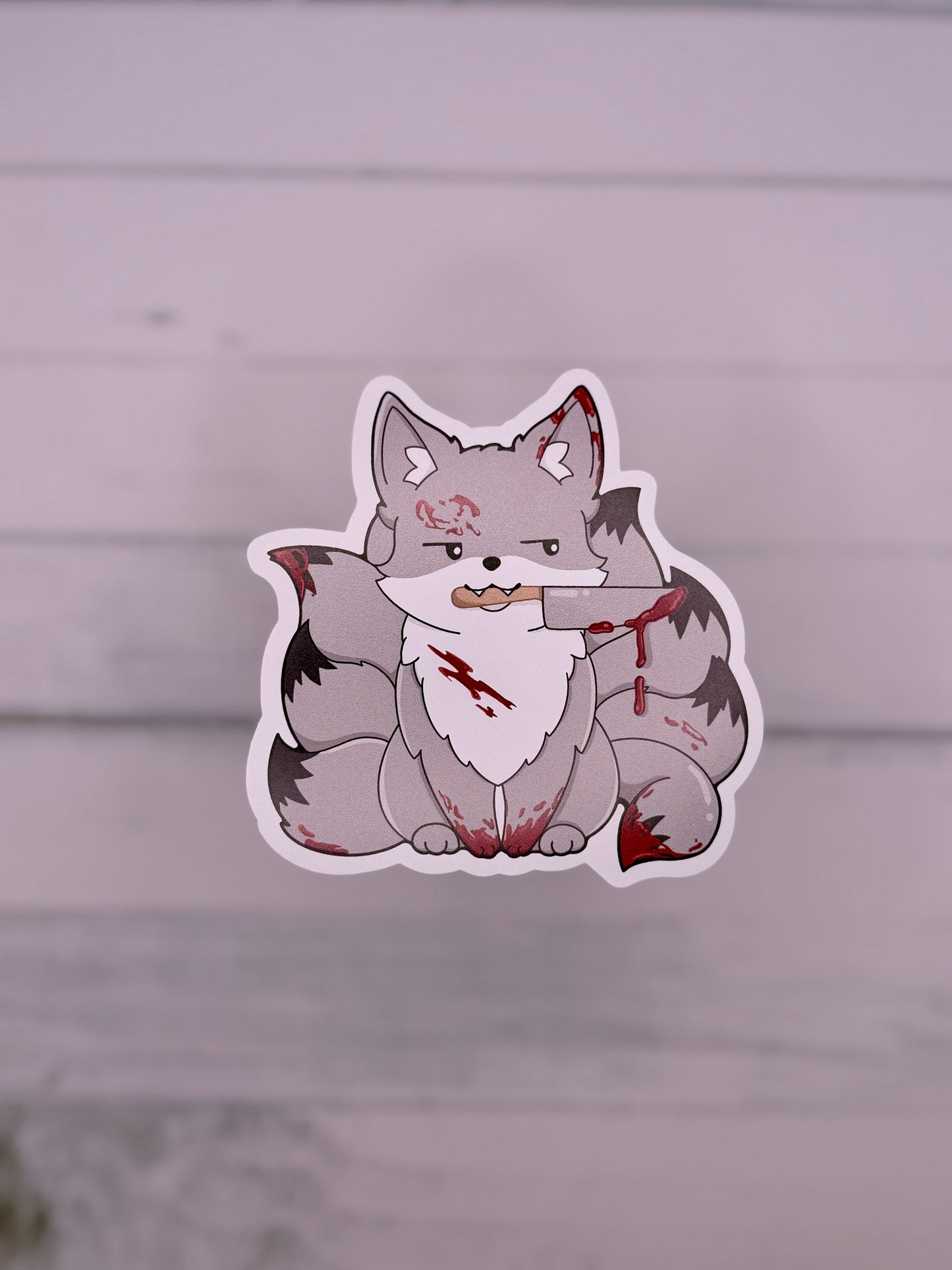 Grey horror themed kitsune sticker with blood splatters and a knife held in its mouth
