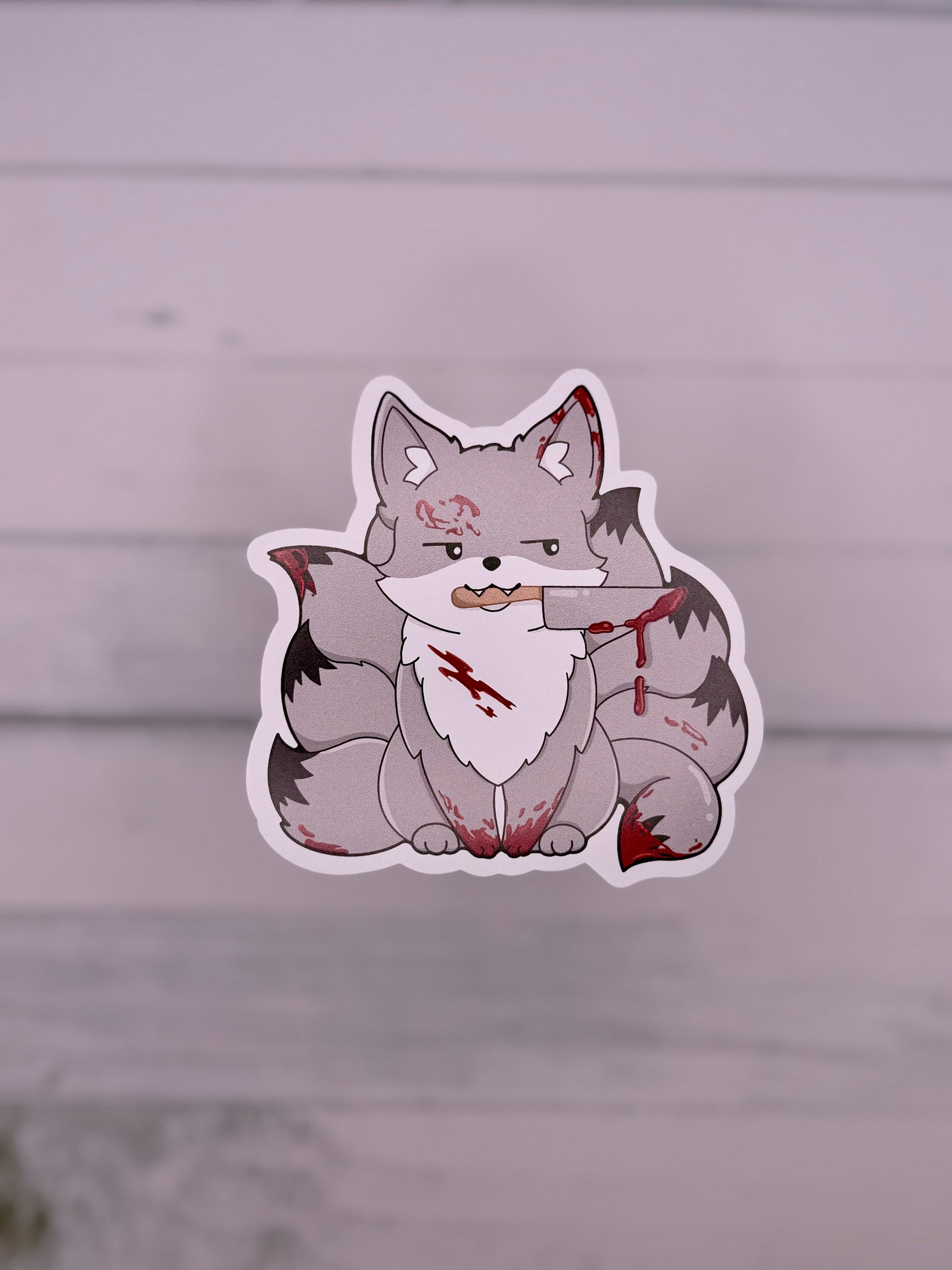 Grey horror themed kitsune sticker with blood splatters and a knife held in its mouth