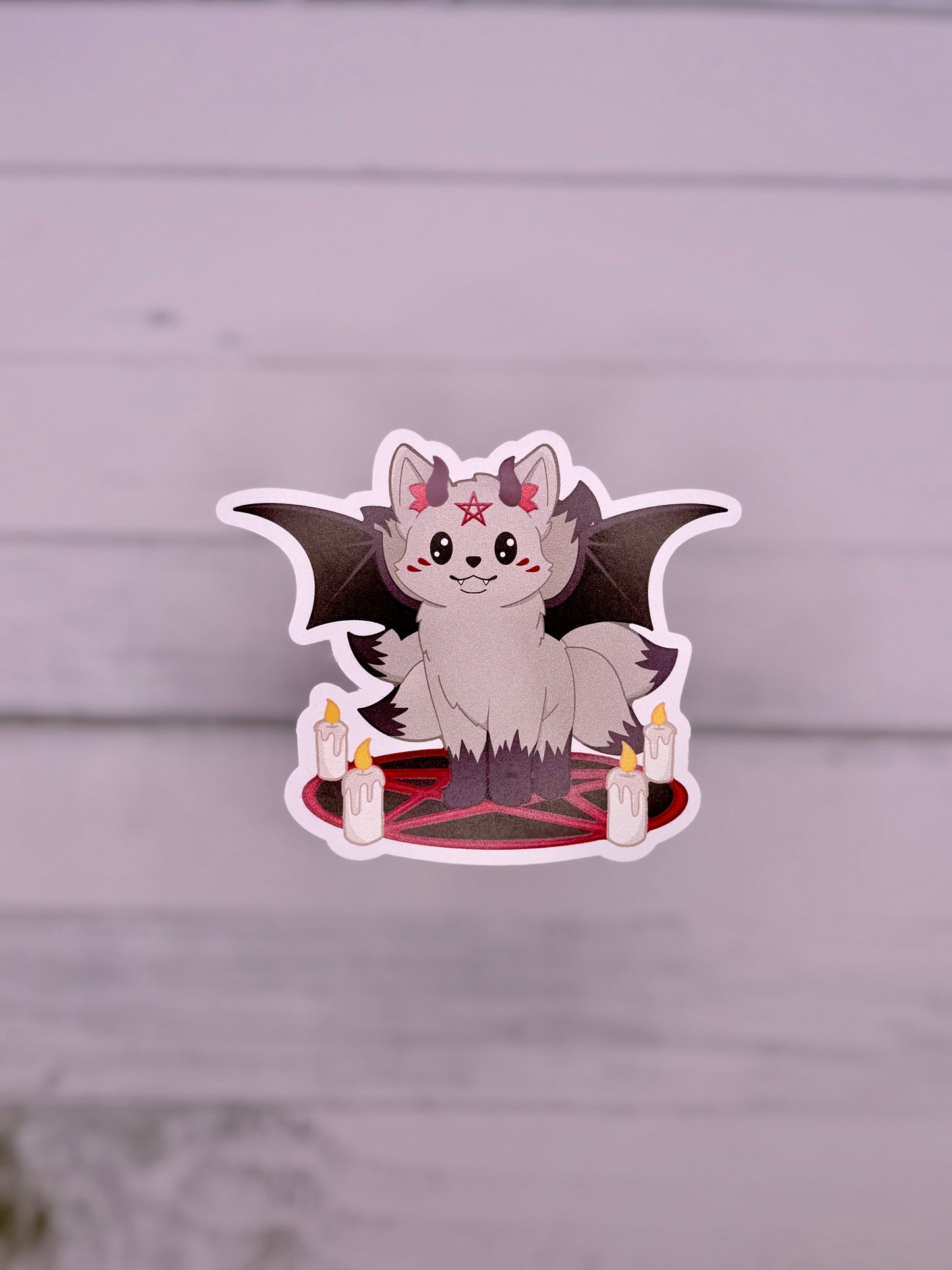 Cute demon kitsune sticker with black bat wings, small horns, candles, and a red pentagram circle