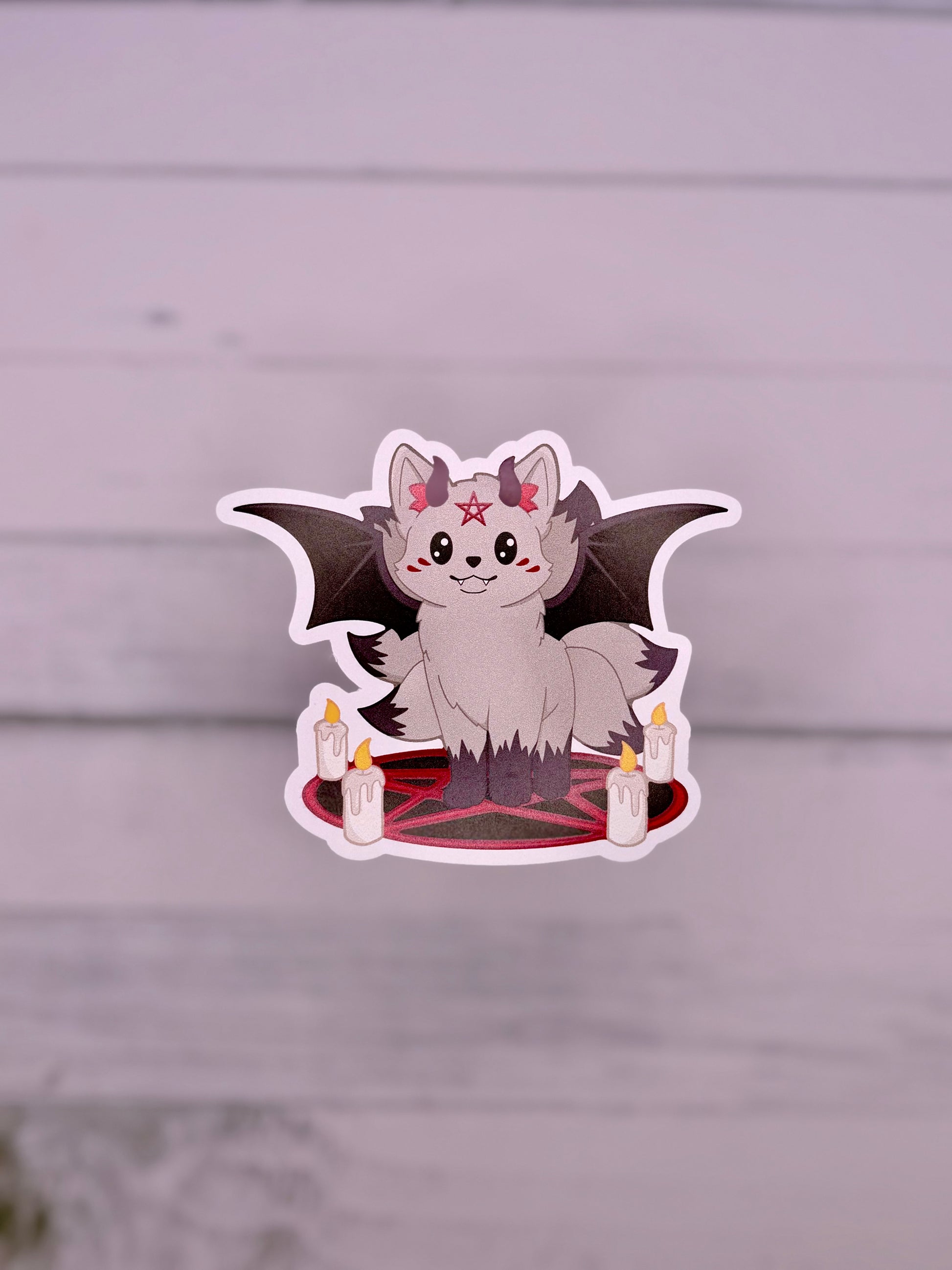 Cute demon kitsune sticker with black bat wings, small horns, candles, and a red pentagram circle