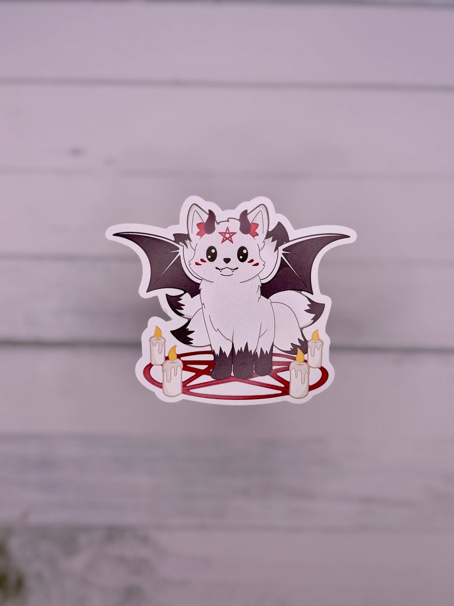 White demon kitsune sticker with black bat wings, small horns, candles, and a red pentagram circle