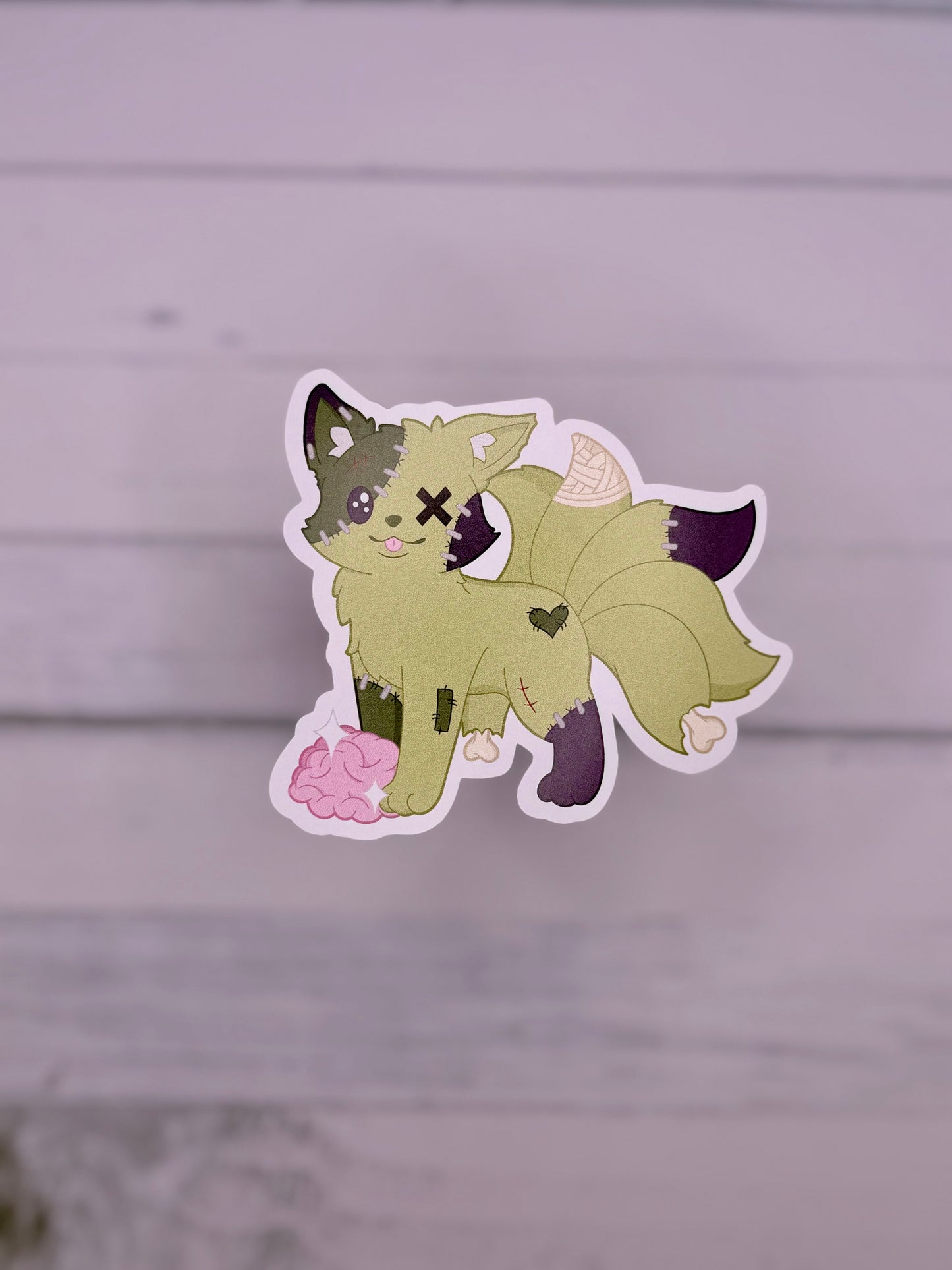 Green stitched zombie kitsune sticker with patchwork details and exposed brain in a cute spooky art style