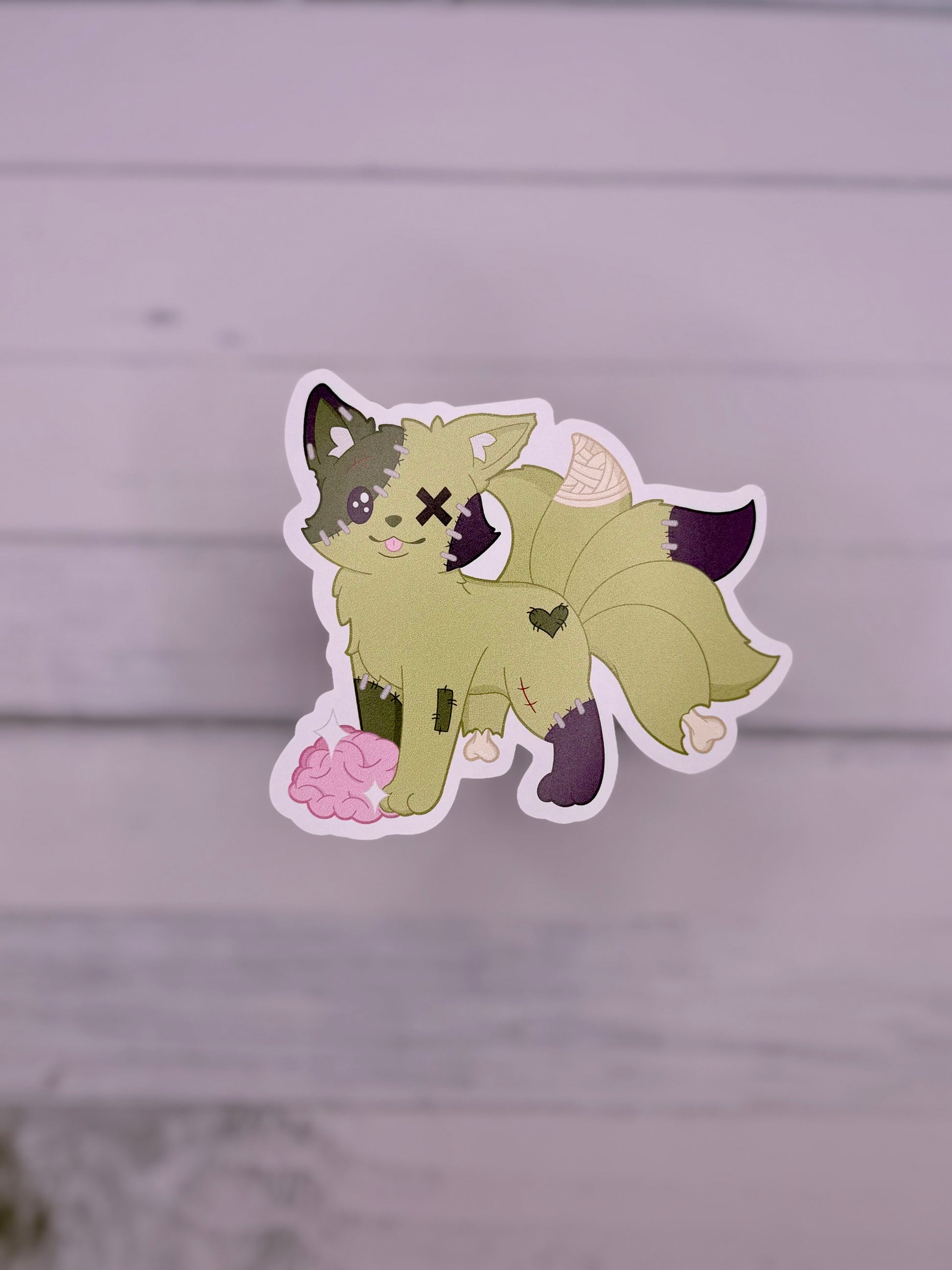 Green stitched zombie kitsune sticker with patchwork details and exposed brain in a cute spooky art style