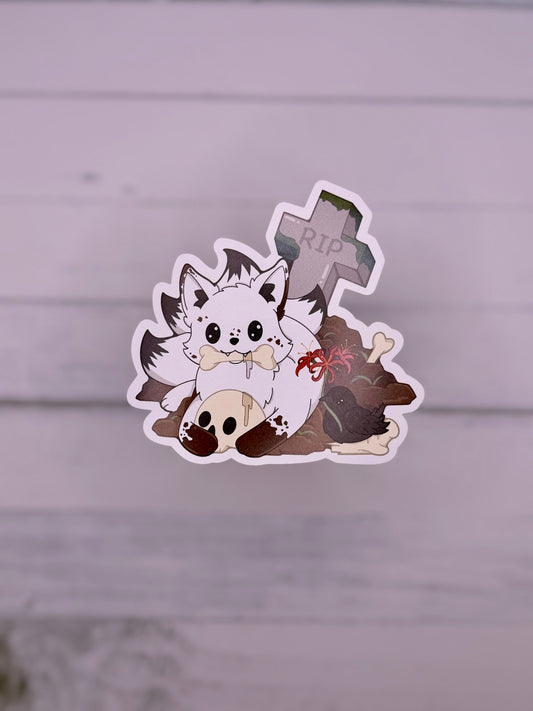 Cute white kitsune sticker sitting in a graveyard with bones, skulls, flowers, and a tombstone