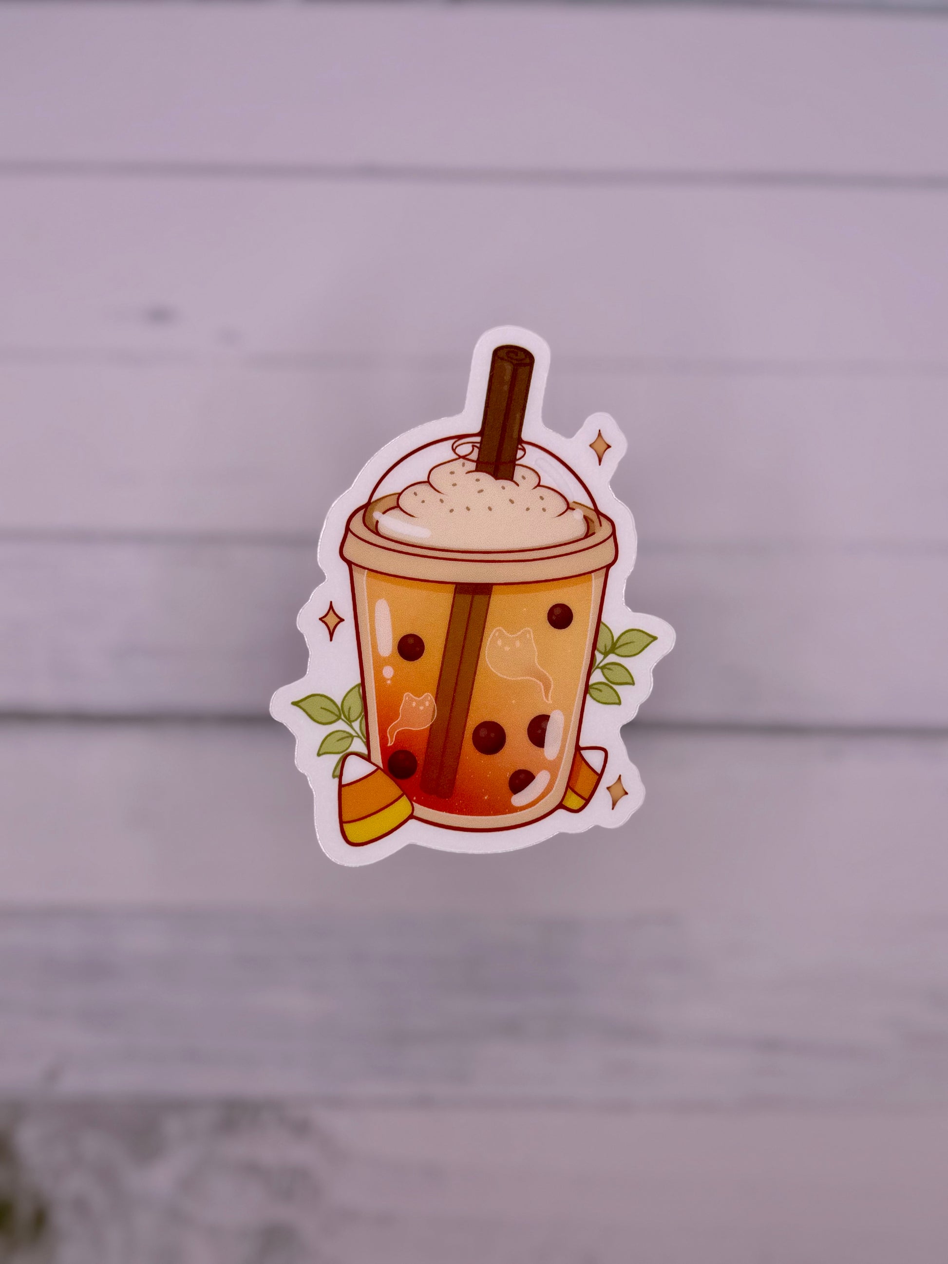 Cute Halloween themed bubble tea sticker featuring an orange milk tea with ghost shapes, boba pearls, whipped topping, cinnamon stick, candy corn, and sparkles