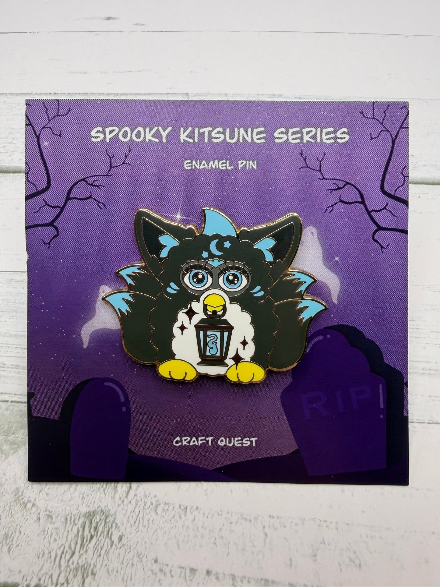 Black and blue retro electronic pet inspired kitsune enamel pin holding a lantern on a purple spooky graveyard backing card
